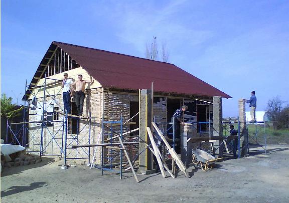 07 sandbag house6.jpg - The walls are coming up! The builders proudly stand near the half-finished home. The sand-filled walls are an excellent sound barrier. Electrical wiring, and radiant floor and wall heat are also very simple to instal.